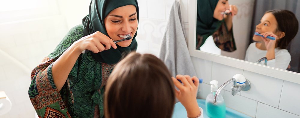 Woman in headscarf brushing her teeth with her daughter. 