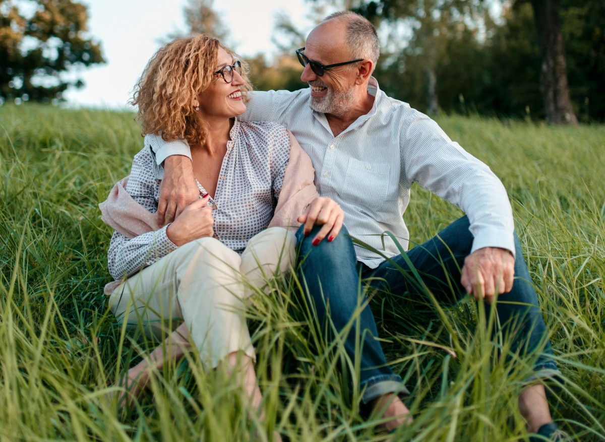 Couple smiling at each other while sitting together in a grassy field